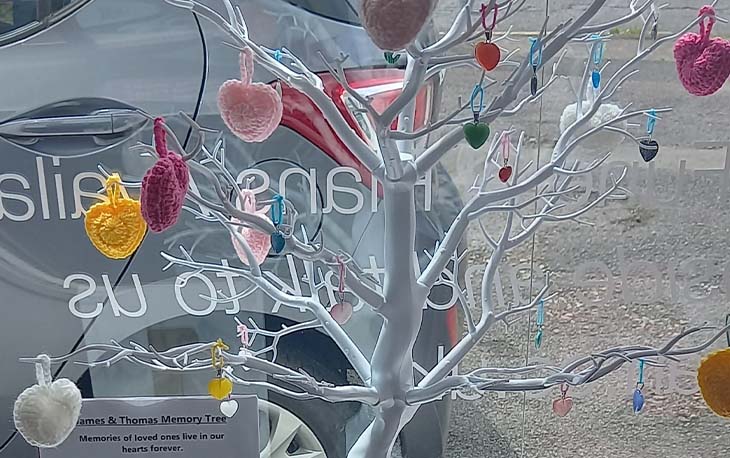 A tree with various coloured crocheted hearts.